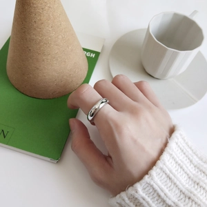 Close-up of minimalist polished sterling silver ring worn on finger with lifestyle props