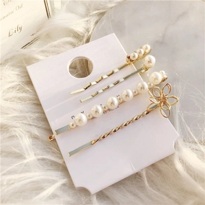 Golden geometric hair clip set with faux pearls and flower details on marble background