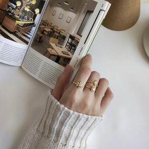 Close-up of gold flower and geometric rings set worn against a magazine background