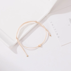 Gros plan d'un bracelet minimaliste en corde tressée crème avec pendentif cœur doré