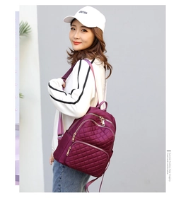 Side view of a purple quilted nylon backpack with gold zippers shown on a female model