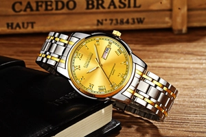 Detail of KINGNUOS two-tone steel watch with golden dial and day-date display window
