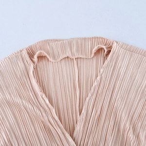 Detailed view of the V-neckline and champagne plisse fabric texture on the jumpsuit