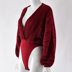 Detail of red long sleeve jumpsuit showing deep V-neck and pleated texture fabric