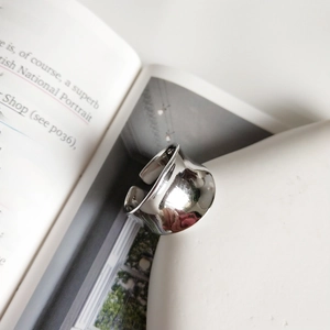 Minimalist wide silver ring with irregular texture displayed against a white ceramic vase
