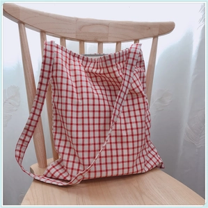 Sac fourre-tout en toile à carreaux rouge et blanc avec bandoulière sur chaise en bois