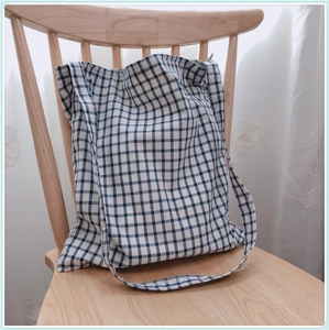 Gros plan du sac fourre-tout à carreaux bleu et blanc posé sur une chaise en bois épurée