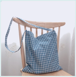 Détail d'un sac cabas en coton à carreaux bleu et blanc suspendu à une chaise en bois