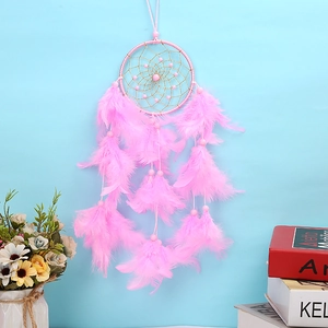 Pink dreamcatcher with soft feathers and beads against a minimalist blue wall