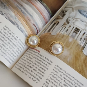 Detail of gold twisted metal border around a large cream pearl earring on a book