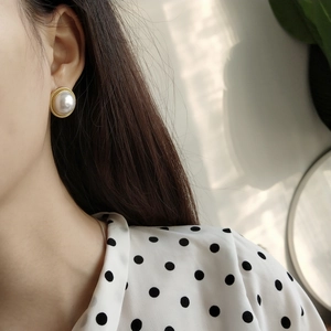 Close-up of a vintage round pearl earring with gold twisted metal edge on model