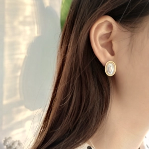 Close-up of a model wearing oval gold earrings with white mother of pearl inlay