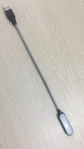 Detail view of portable USB LED light with flexible metal hose and black casing on wood