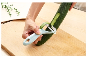 Close-up of a light blue ceramic peeler peeling a fresh cucumber on wooden board