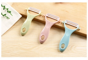 Three colorful ceramic vegetable peelers in pink, green, and blue on a wooden cutting board
