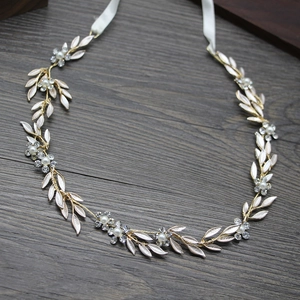 Détail d'un bandeau de mariée avec feuilles dorées, perles et strass sur ruban blanc