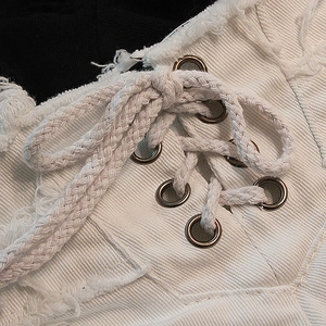 Dettaglio degli hot pants in denim bianco con bordi sfrangiati, occhielli e lacci