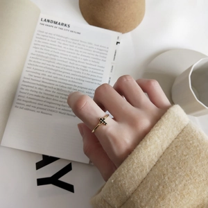 Close-up of a delicate gold cross ring with black diamonds worn by a model in a cozy setting