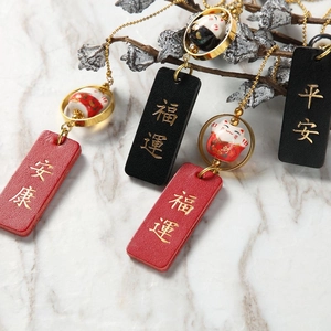 Detail of ceramic Maneki-neko lucky charm with leather tag and gold metal ring