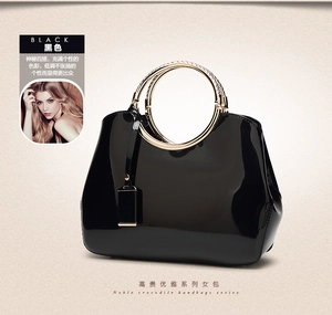 Detail of glossy black patent leather handbag with woven gold metal ring handles