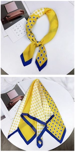 Detail of yellow silk scarf with blue trim, polka dots and floral print on white prop