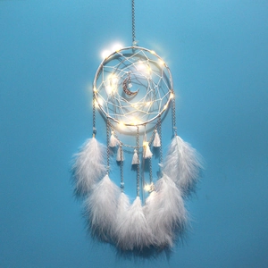 Detail of dream catcher with white feathers, crescent moon pendant and warm LED string lights
