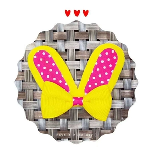 Pink and yellow bunny ears hair accessory with polka dots and ribbon bow on a woven mat