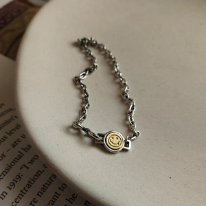 Detail of a 925 sterling silver chain bracelet with a gold smiley face charm on a tray
