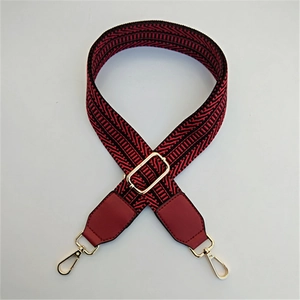 Close-up of red and black woven bag strap with golden metal clips and leather ends