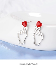 Close-up of silver hand gesture stud earrings with red heart drip oil finish on ceramic