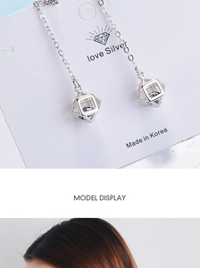 Macro detail of long silver chain earrings with cubic zirconia hollow cube pendants