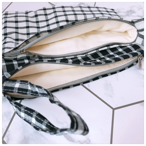 Detailed interior view of checkered canvas bag featuring dual zipper compartments and strap