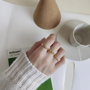 Detail of elegant gold chain ring with T-bar design on a white knit sweater sleeve