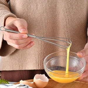 Mini stainless steel spring whisk mixing egg yolks in a bowl for baking preparation