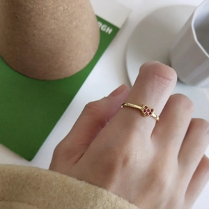 Detail showing a gold heart ring with red stones worn on hand with a soft background