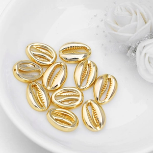 Close-up of ten gold-colored shell charms on white ceramic plate for DIY jewelry making