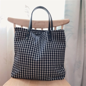 Navy blue checkered canvas tote bag with black faux leather handles on a wooden chair