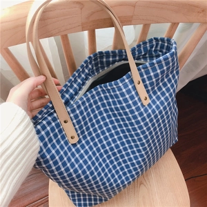 Detail of blue gingham canvas tote bag with leather straps and secure zipper closure
