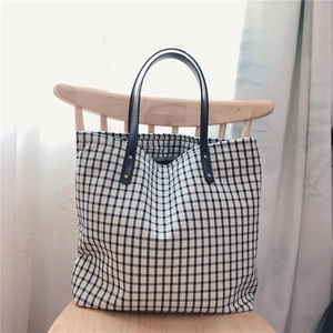 Detail of checkered canvas tote bag with black faux leather handles on a wooden chair