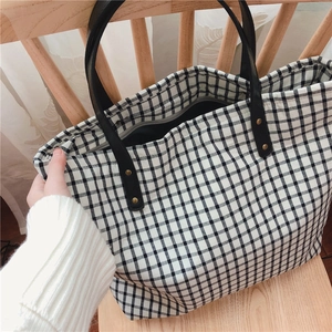 Close-up of black and white gingham tote bag with gold rivets on a wooden chair