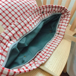 Detail view of red gingham tote bag featuring a secure zipper and metal snap closure