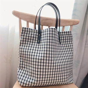 Detailed view of checkered cotton tote bag with leather handles on a wooden chair