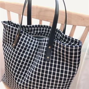 Detail of checkered tote bag with black leather straps and secure zipper closure