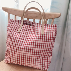 Close-up of red and white checkered cotton tote bag on a wooden chair by a window