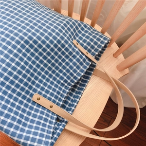 Detailed close-up of blue gingham cotton tote bag with leather straps and rivet accents