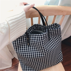 Detail of black and white gingham tote bag with leather straps and gold rivets