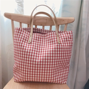 Detail of red gingham cotton tote bag with leather straps and metal rivets on a chair