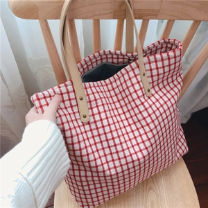 Detail of red and white checkered canvas tote bag with brown leather handles on wooden chair