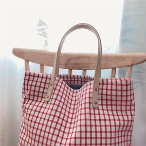 Detail of red checkered canvas tote with leather handles on a wooden chair