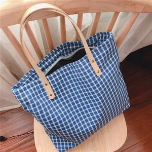Detail of blue and white checkered canvas tote bag with brown leather handles and zipper